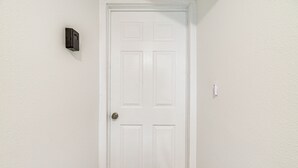A white door with a simple design, a small wall-mounted device to the left, and a light switch to the right. - 'the Penthouse' in Space City: 10 Mi to NRG (Houston)