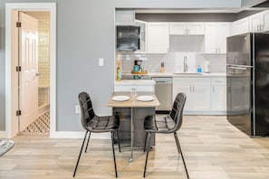 A modern kitchen with white cabinets, a black refrigerator, and a dining area with two chairs and a table. - 'the Penthouse' in Space City: 10 Mi to NRG (Houston)