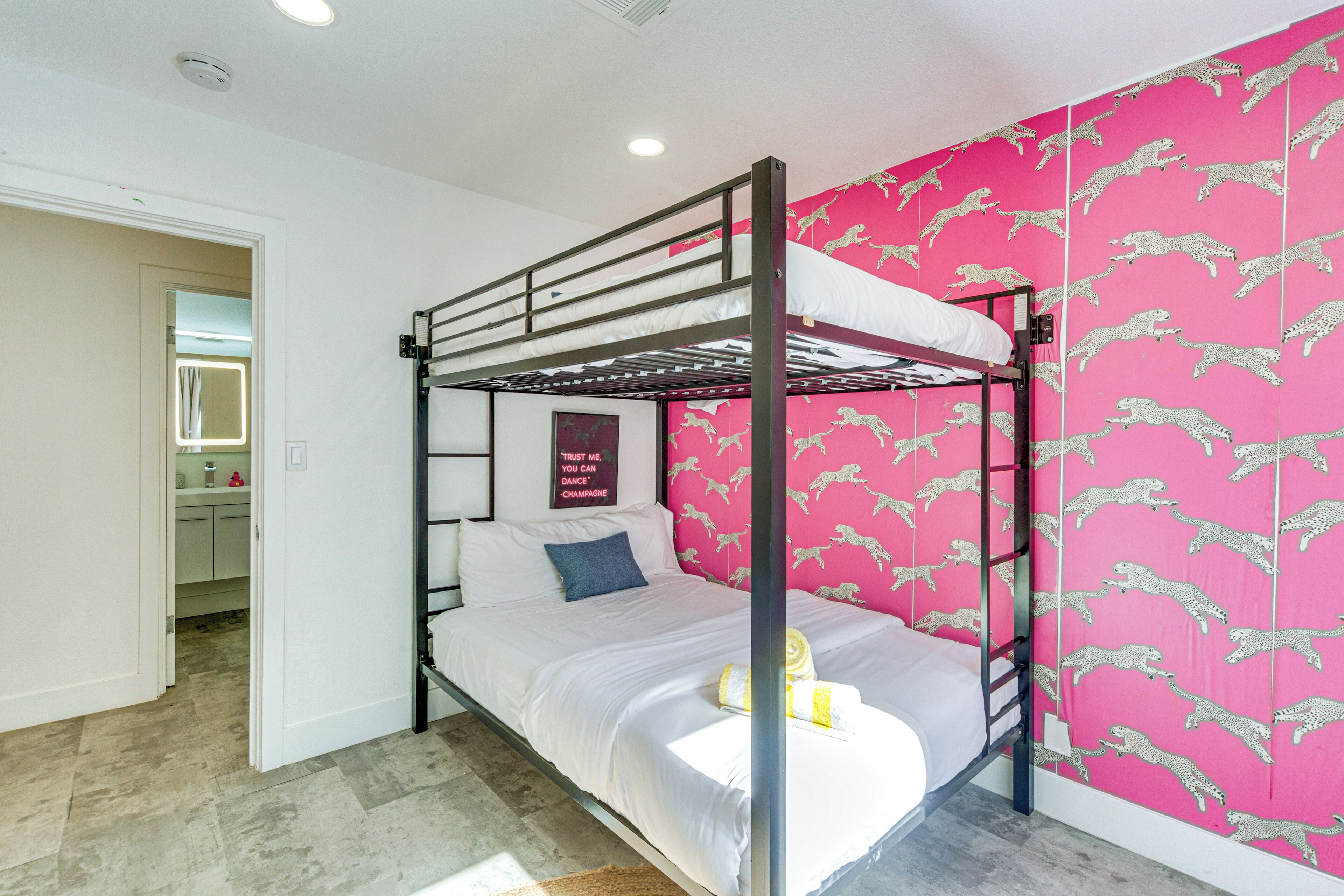 Habitación con literas, pared con estampado de leopardo rosa, una mesita de noche pequeña y un espejo sobre la puerta.