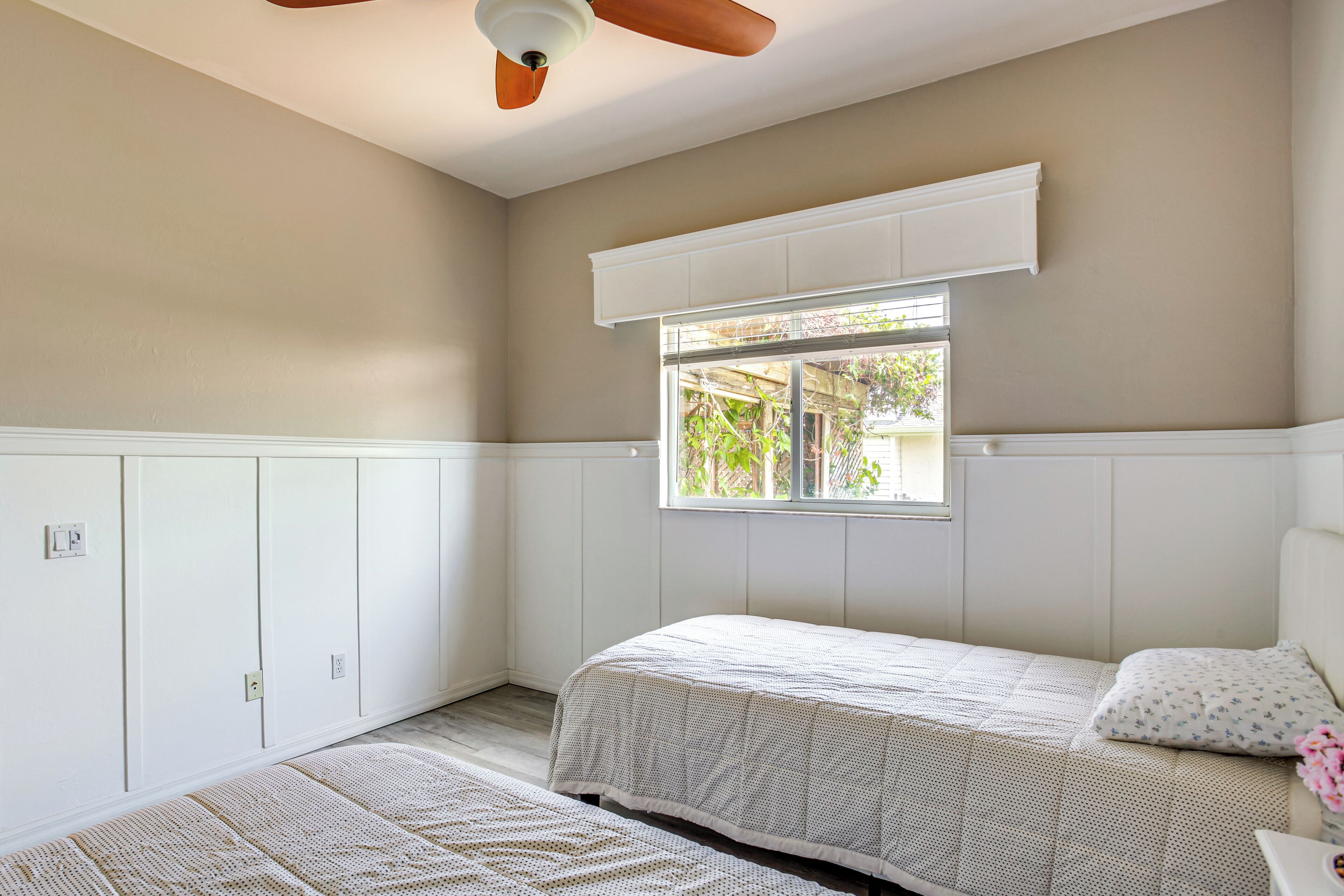Une chambre avec deux lits, une fenêtre, un ventilateur de plafond et des placards intégrés.