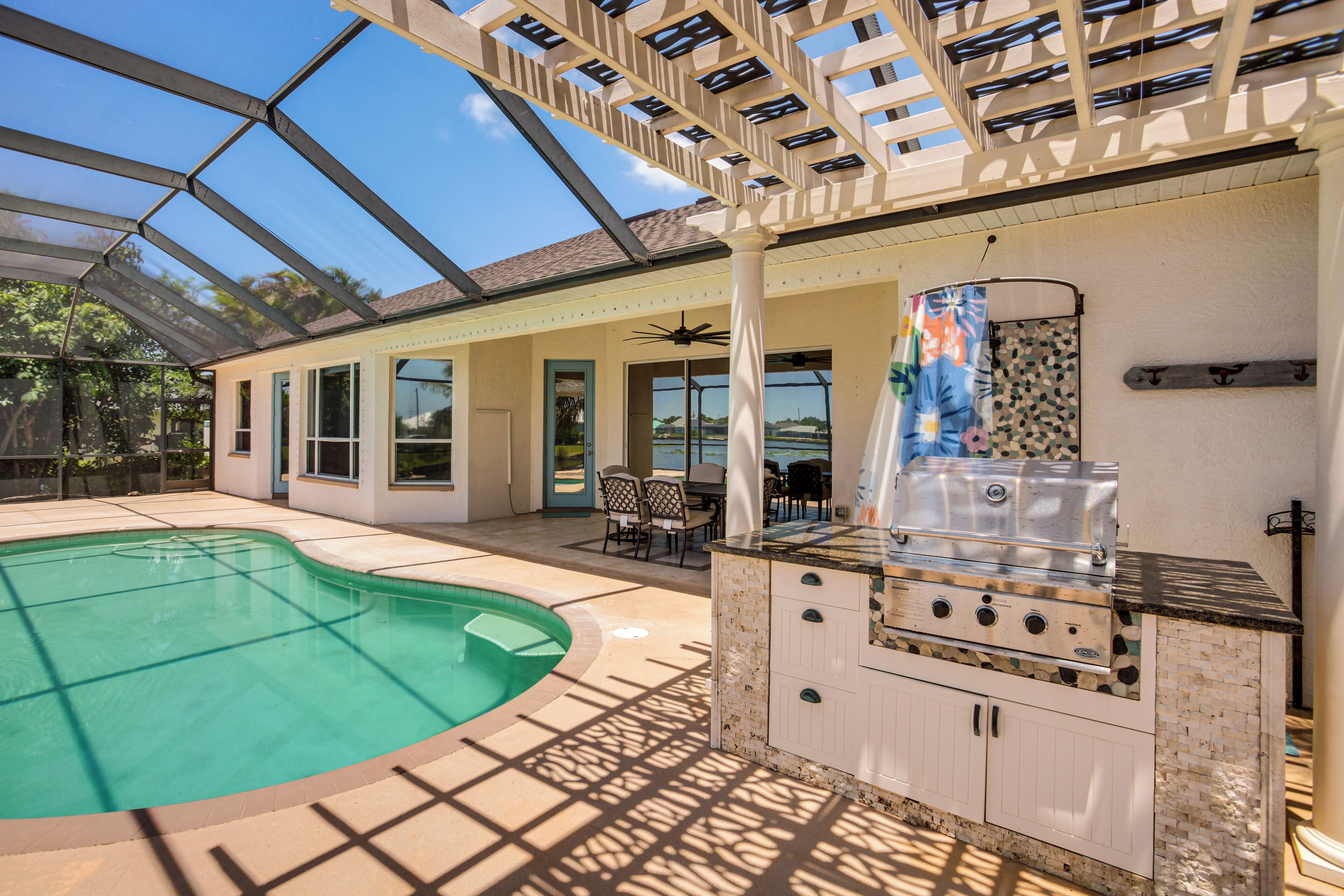 A covered outdoor area with a swimming pool, a barbecue station, and a patio with chairs and a table.