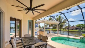 Un patio cubierto con piscina, mobiliario exterior y vistas a un barrio residencial.