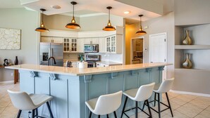 Una cocina moderna con una isla central, taburetes de bar, iluminación colgante y vistas al área de comedor.