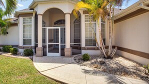 Una casa de dos pisos con un porche cubierto, una palmera y un césped bien cuidado.