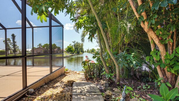 Una terraza de madera que conduce a una estructura de vidrio con vistas a un río, rodeada de exuberante vegetación.