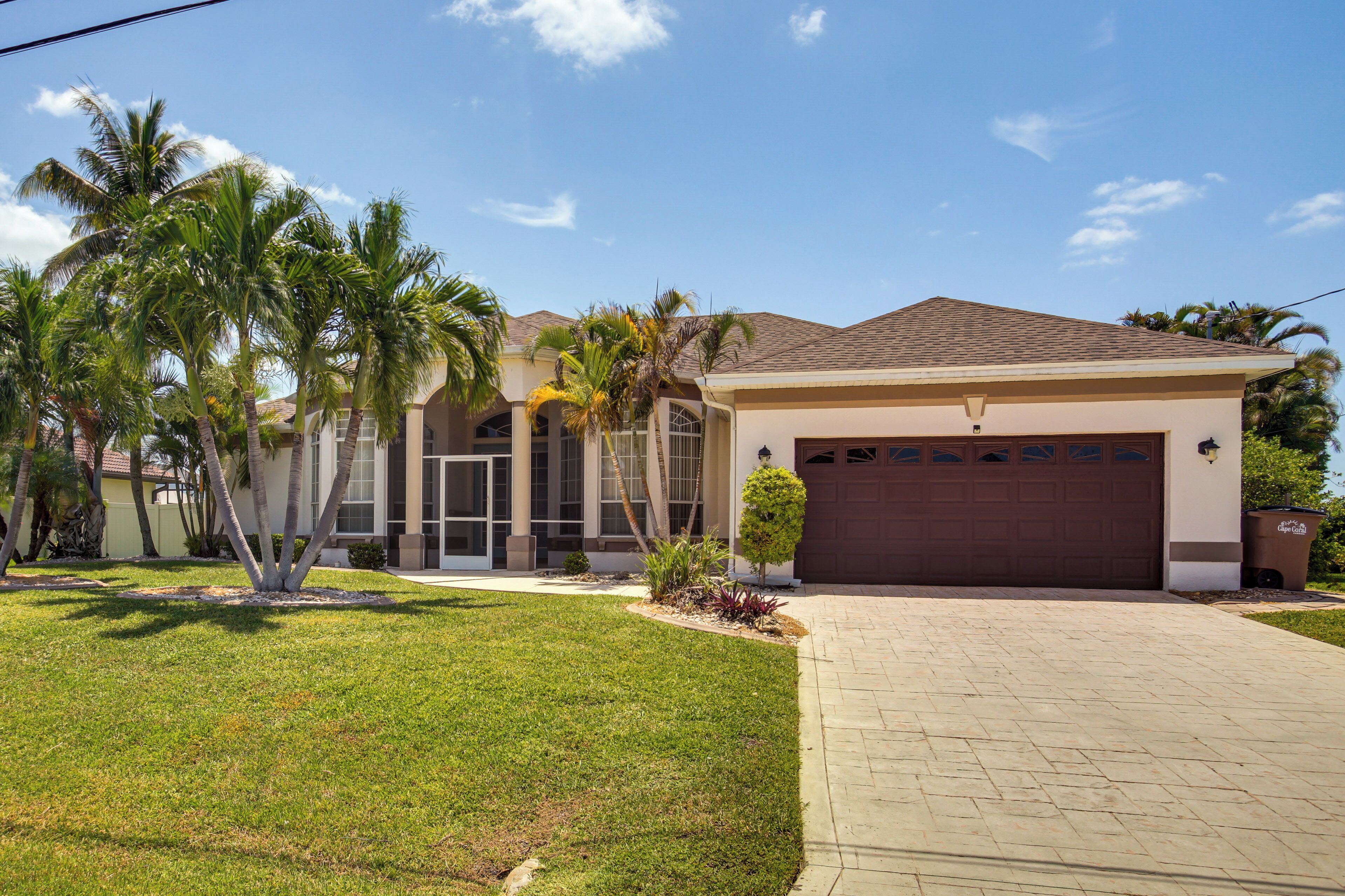 A residential house with a garage, a well-maintained lawn, and palm trees.