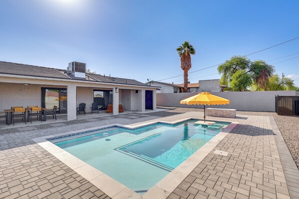 A swimming pool with a tiled deck, a yellow umbrella, and a palm tree in the background.