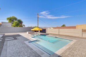 A rectangular swimming pool with a tiled deck, surrounded by a low wall and a clear blue sky.