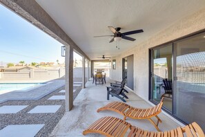 A covered outdoor area with a pool, lounge chairs, ceiling fans, and a table with chairs.