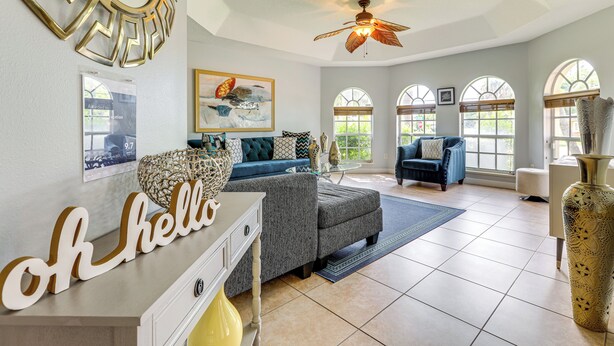 A spacious living room with a high ceiling, a ceiling fan, and large windows. - Family Home in Port St Lucie w/ Furnished Pergola! (Port Saint Lucie)