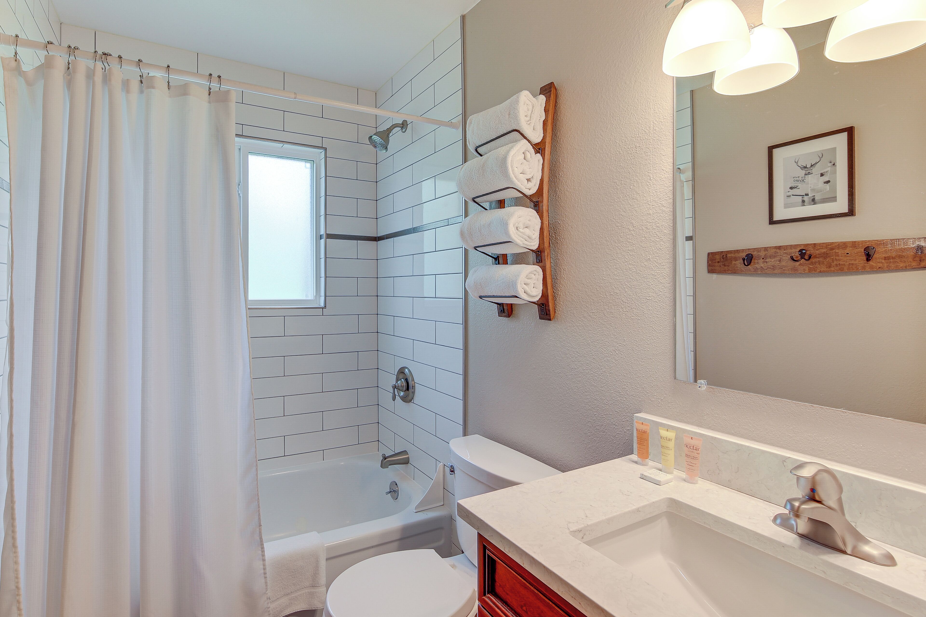 Une salle de bain moderne avec une baignoire, des toilettes et un lavabo. On y trouve des serviettes sur un porte-serviettes et un tableau encadré au mur.