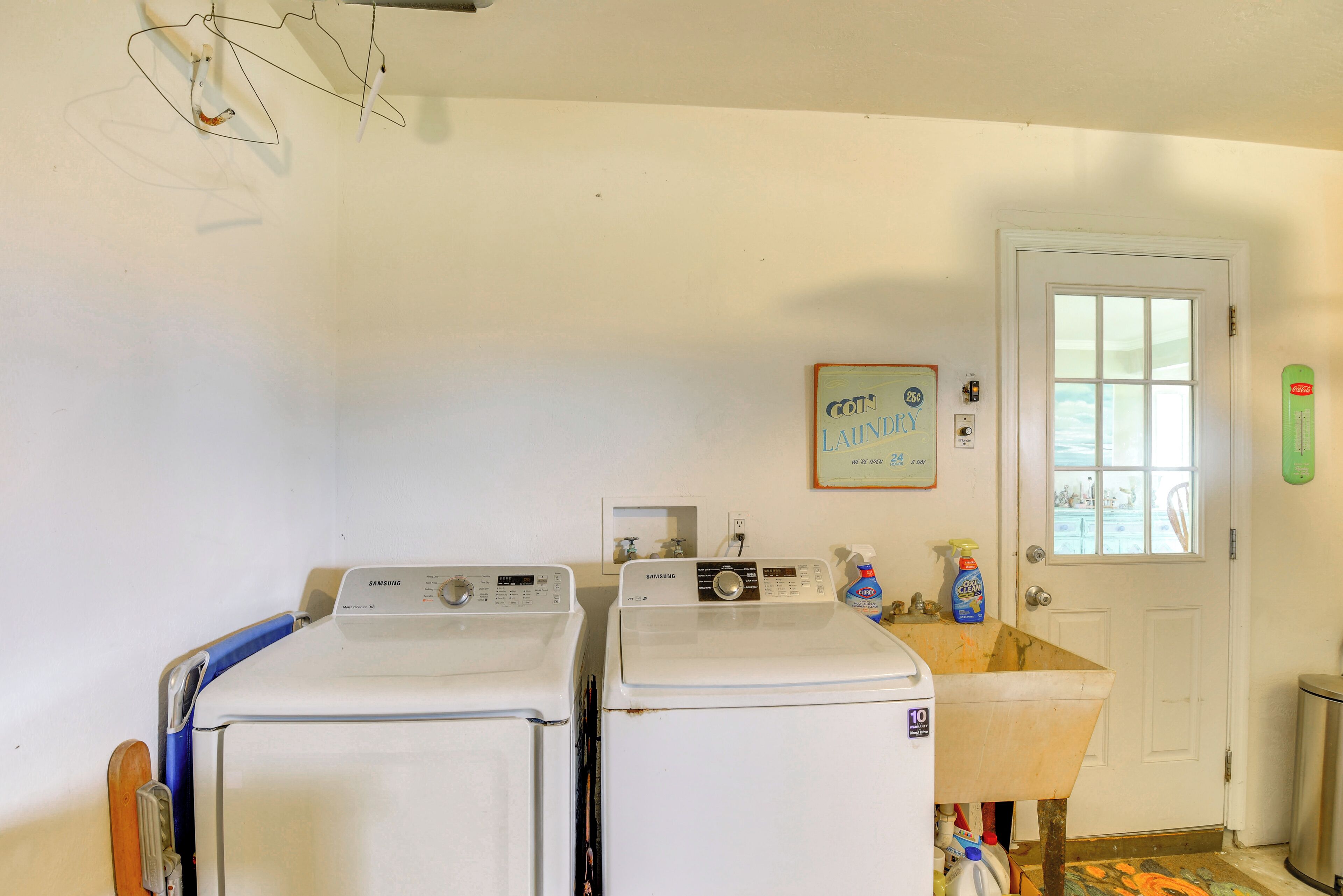 A laundry room with two white washing machines, a door with a window, and a sign indicating the laundromat is open 24 hours.