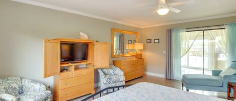 A bedroom with a bed, two dressers, a television, a ceiling fan, and a window with curtains.