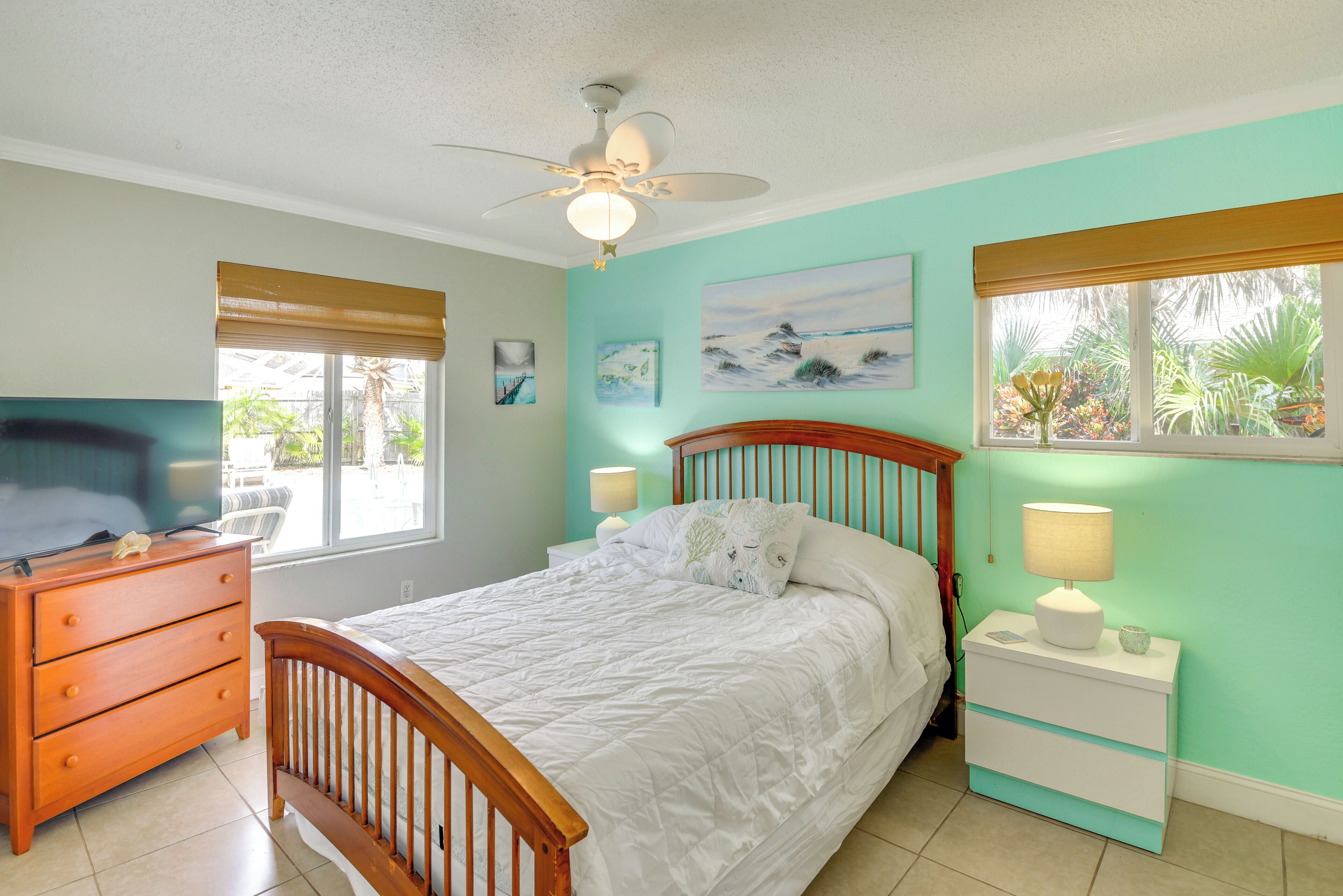A bedroom with a bed, wooden dresser, nightstands, a ceiling fan, and two windows with blinds.