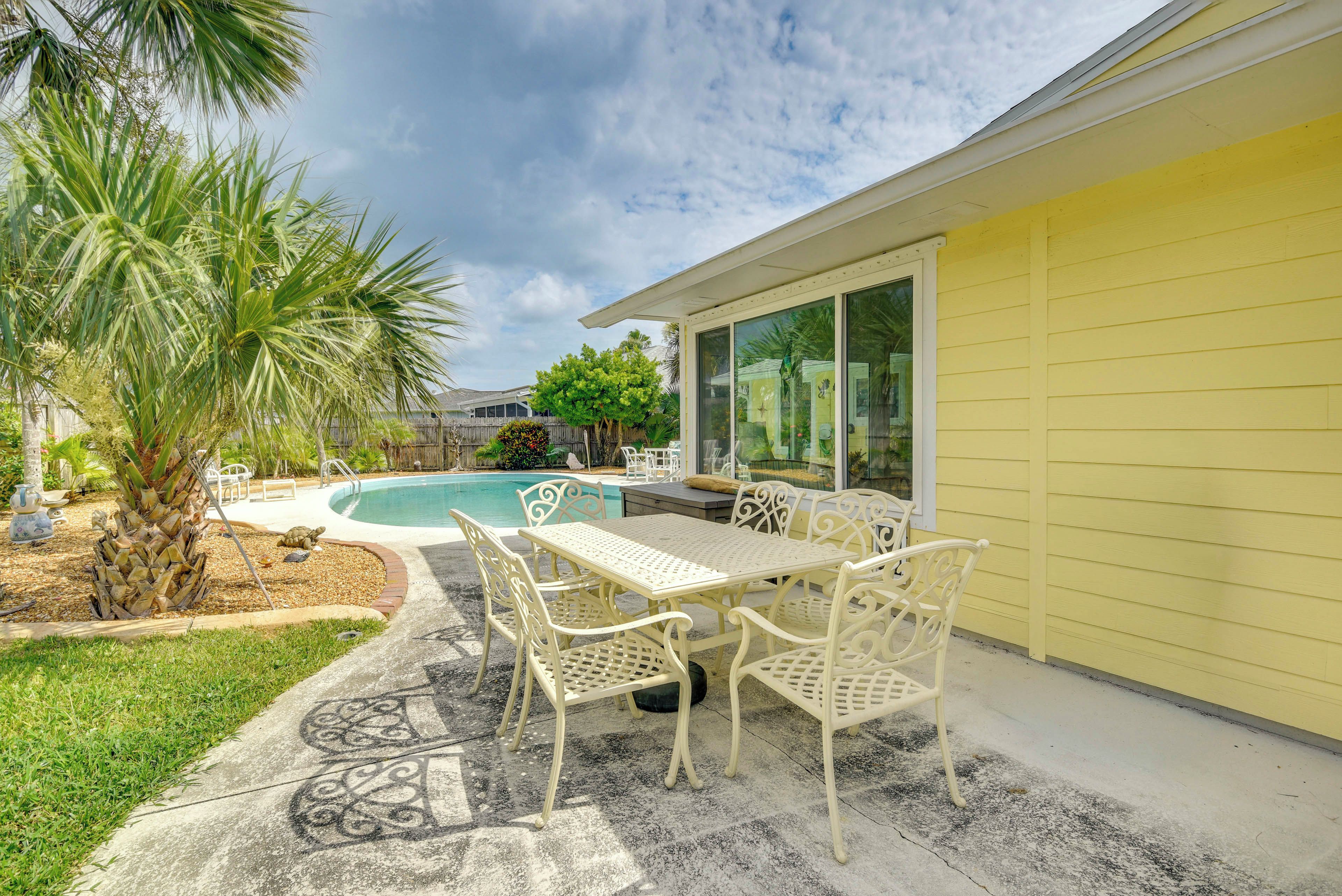 A patio with a table and chairs, a swimming pool, and a yellow building.