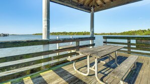 Un muelle de madera con una mesa de picnic y bancos, con vista a una masa de agua y una orilla lejana.