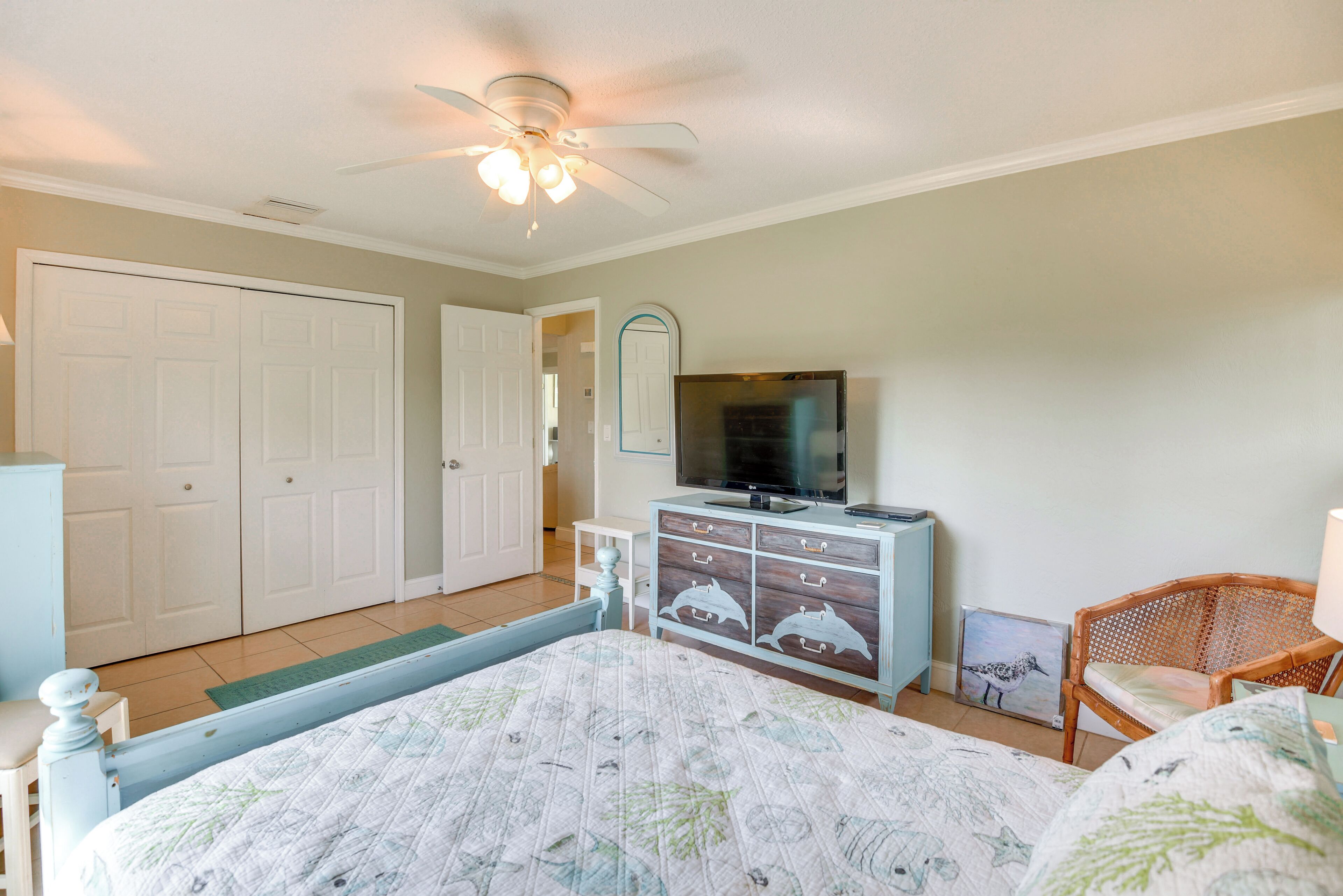A bedroom with a bed, a dresser, a television, and a ceiling fan.