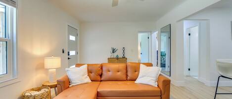 Una sala de estar moderna con un sofá modular, una mesa de centro redonda, un ventilador de techo y un ventanal grande.