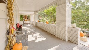 Μια σκεπαστή βεράντα με τοίχο από τούβλα, ένα παγκάκι και κολοκύθες.