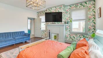 A bedroom with a large bed, a blue sofa, a fireplace, and a TV.