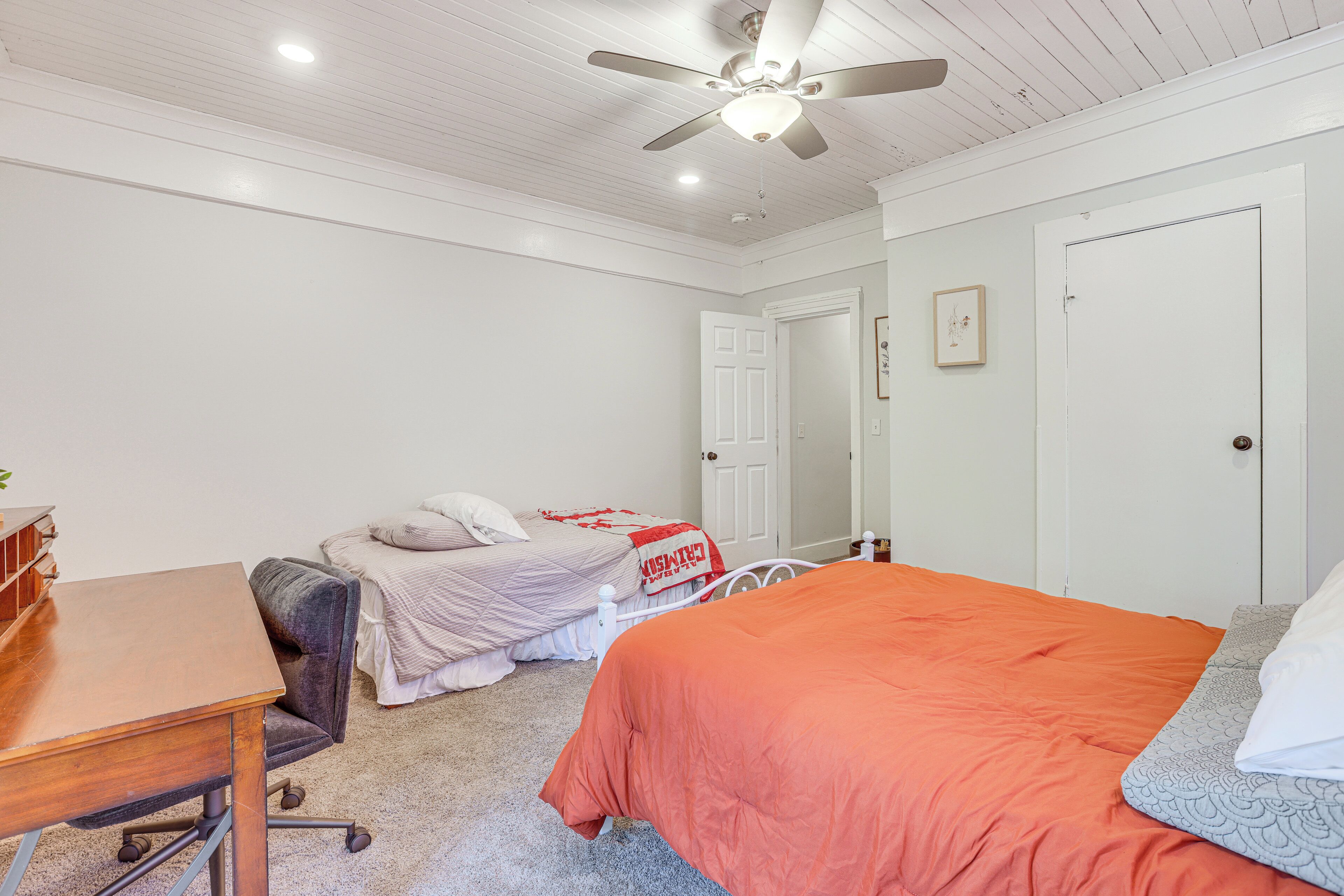 Een slaapkamer met twee bedden, een bureau en een plafondventilator.