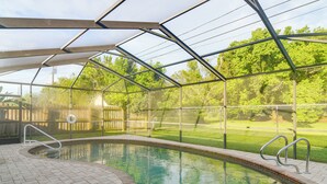 Une piscine intérieure dotée d’un toit en verre, entourée d’une terrasse en briques et de rampes en métal.