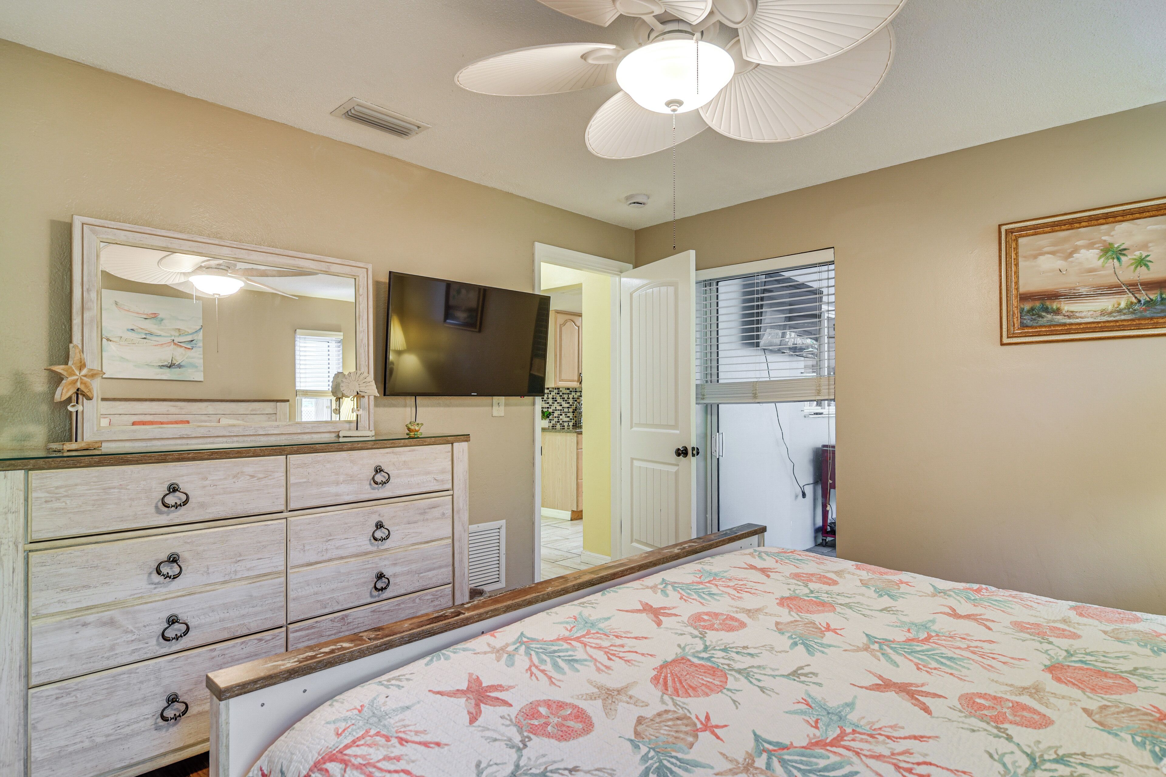 A bedroom with a bed, dresser, ceiling fan, and a door leading to another room.