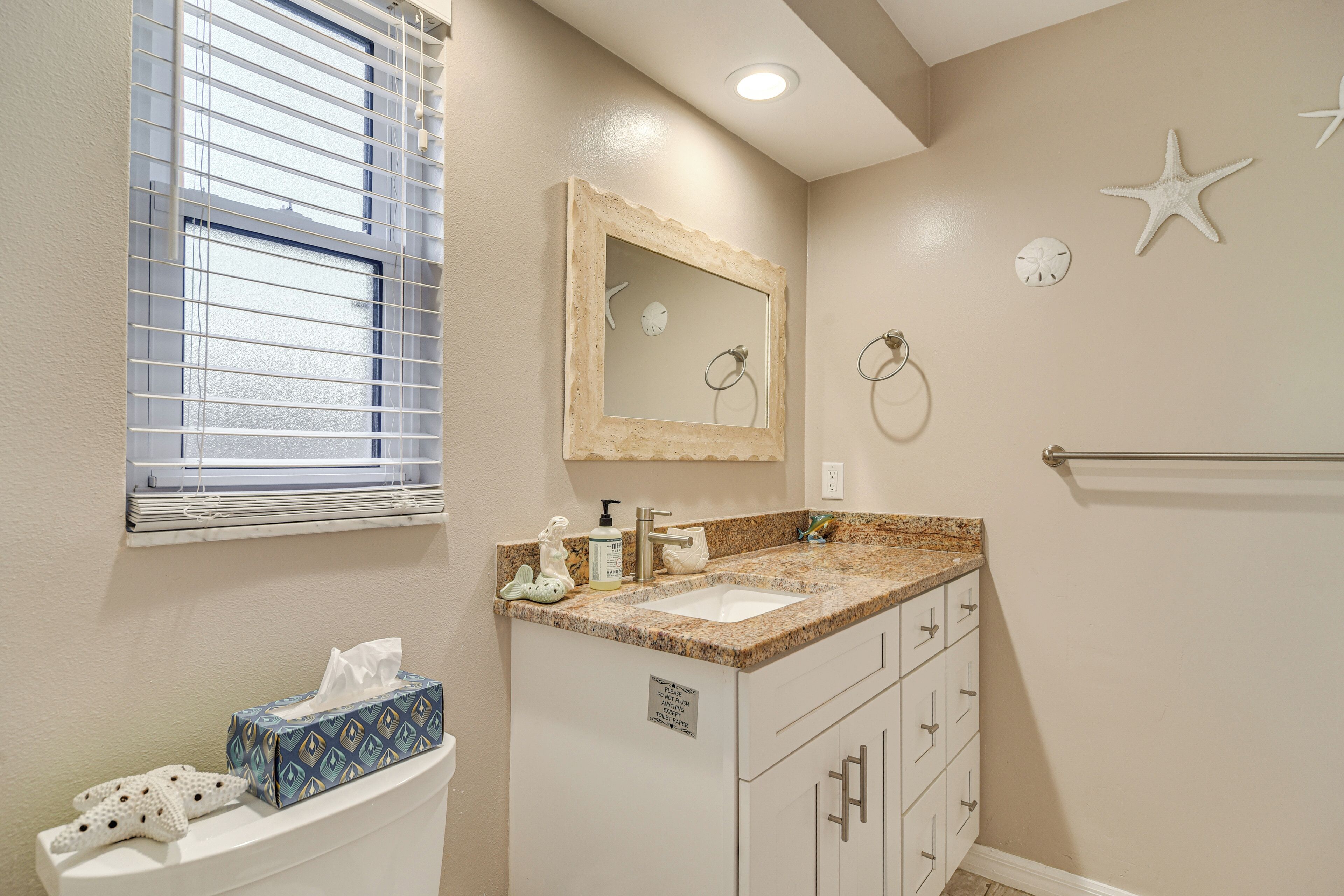 A bathroom with a vanity, sink, mirror, towel rack, and a window with blinds.