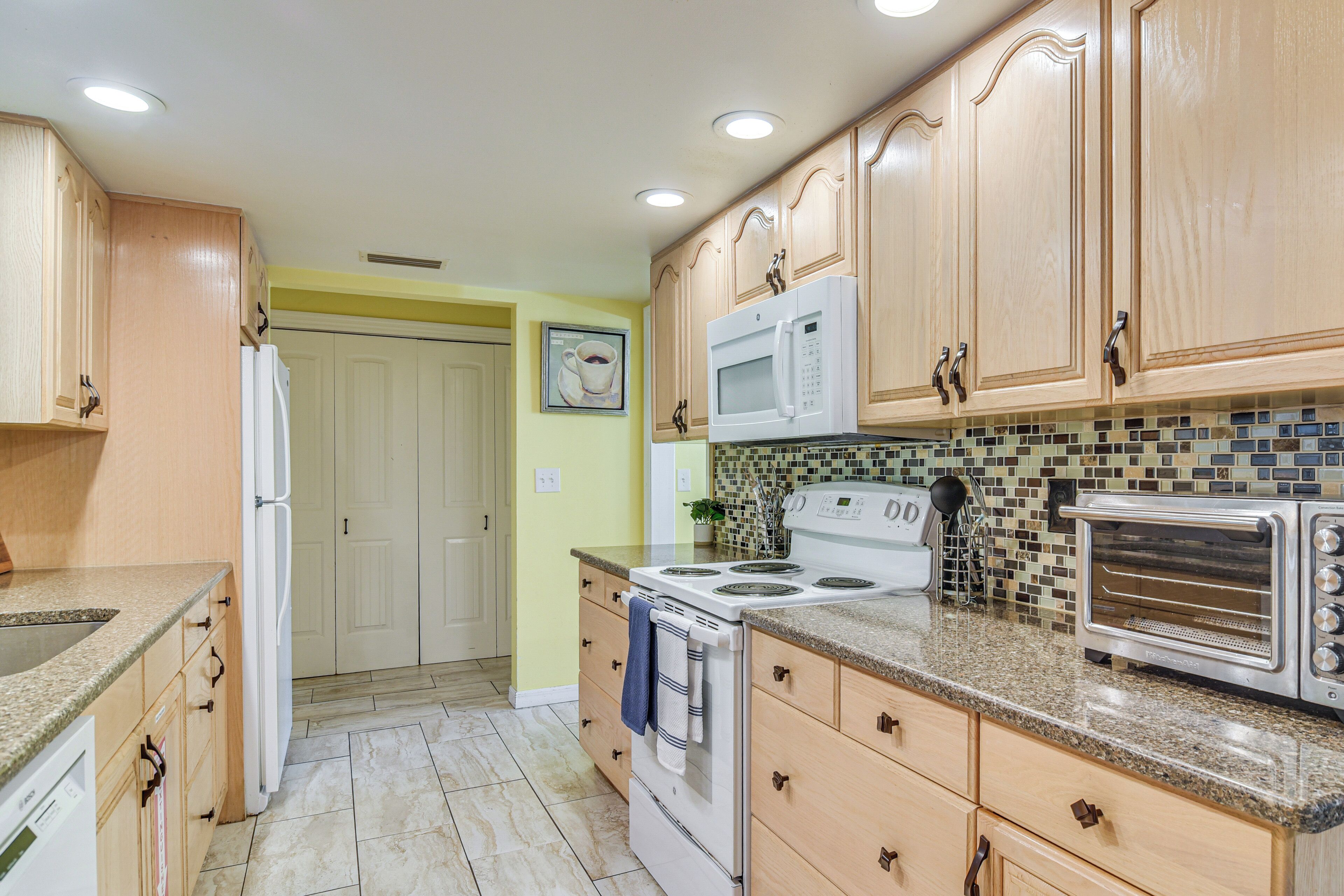 A kitchen with wooden cabinets, a white refrigerator, a stove, a microwave, and a toaster oven.