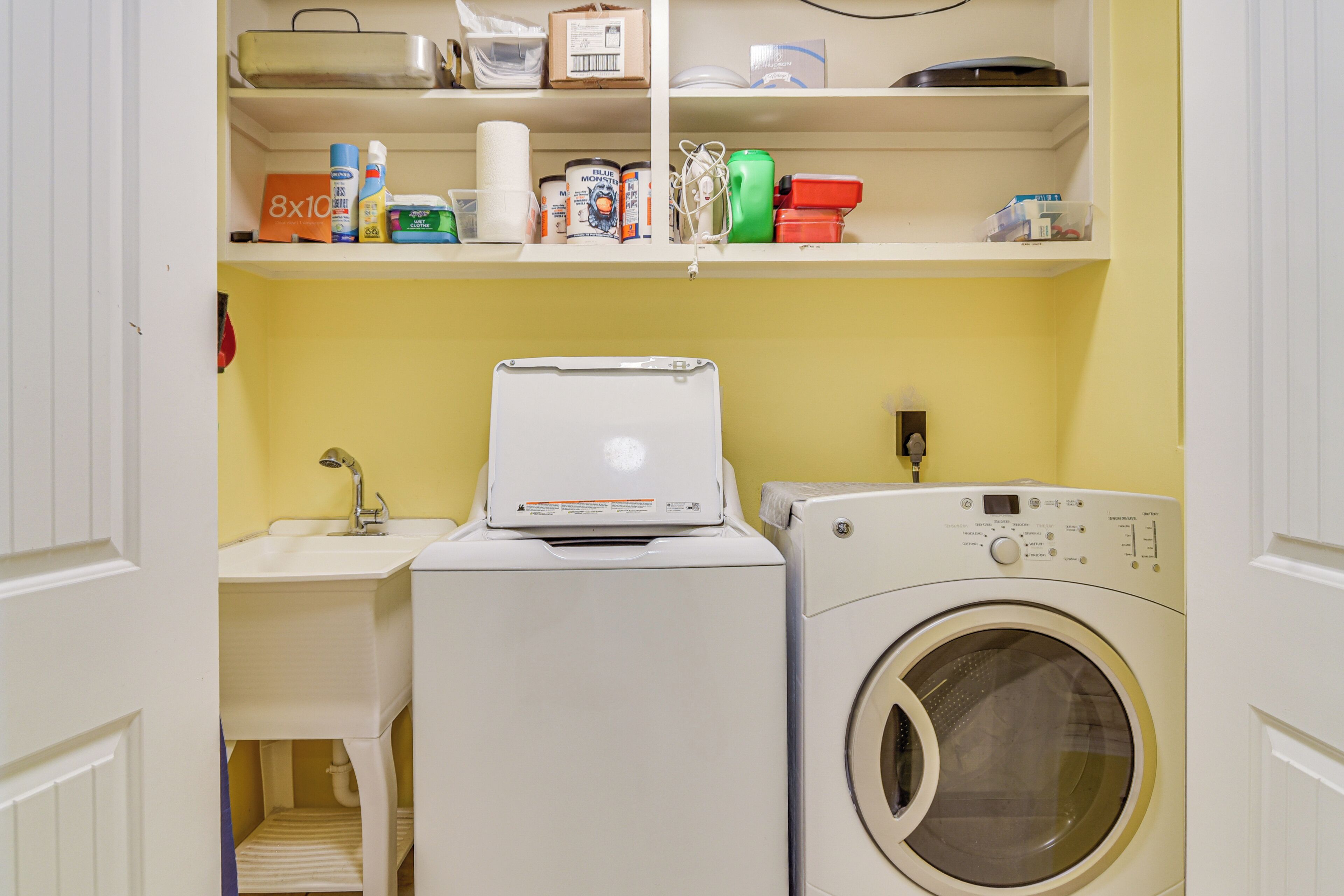 Un espace buanderie compact comprenant un lave-linge, un sèche-linge et des étagères au-dessus, où sont rangés divers objets.