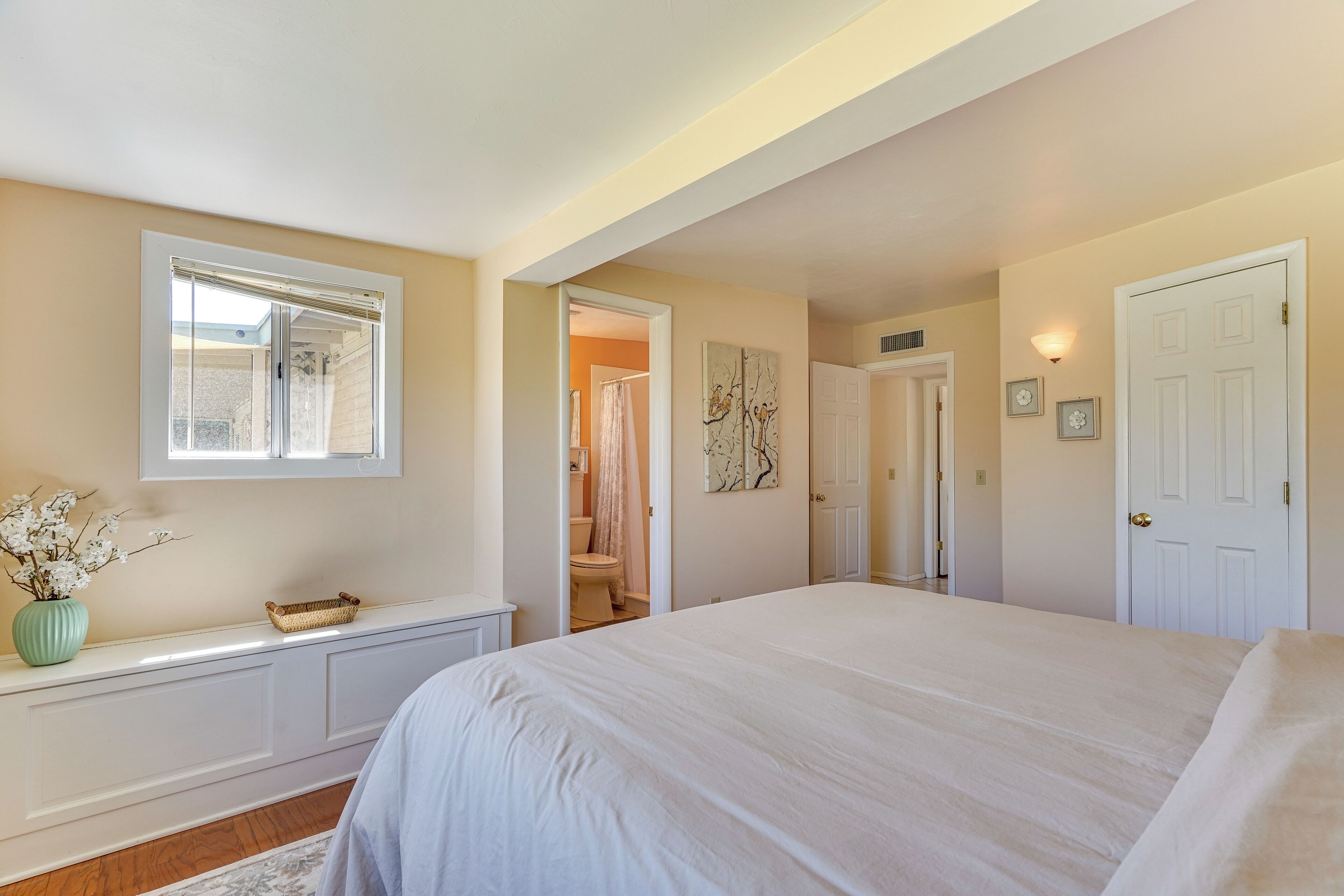 Une chambre à coucher avec un grand lit, une fenêtre, une coiffeuse et une porte donnant sur une salle de bain.