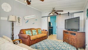 A living room with a brown leather sofa, a television on a wooden cabinet, and a ceiling fan.