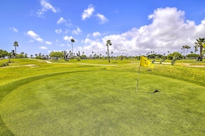 A golf course with well-maintained grass, palm trees, and a clear sky.