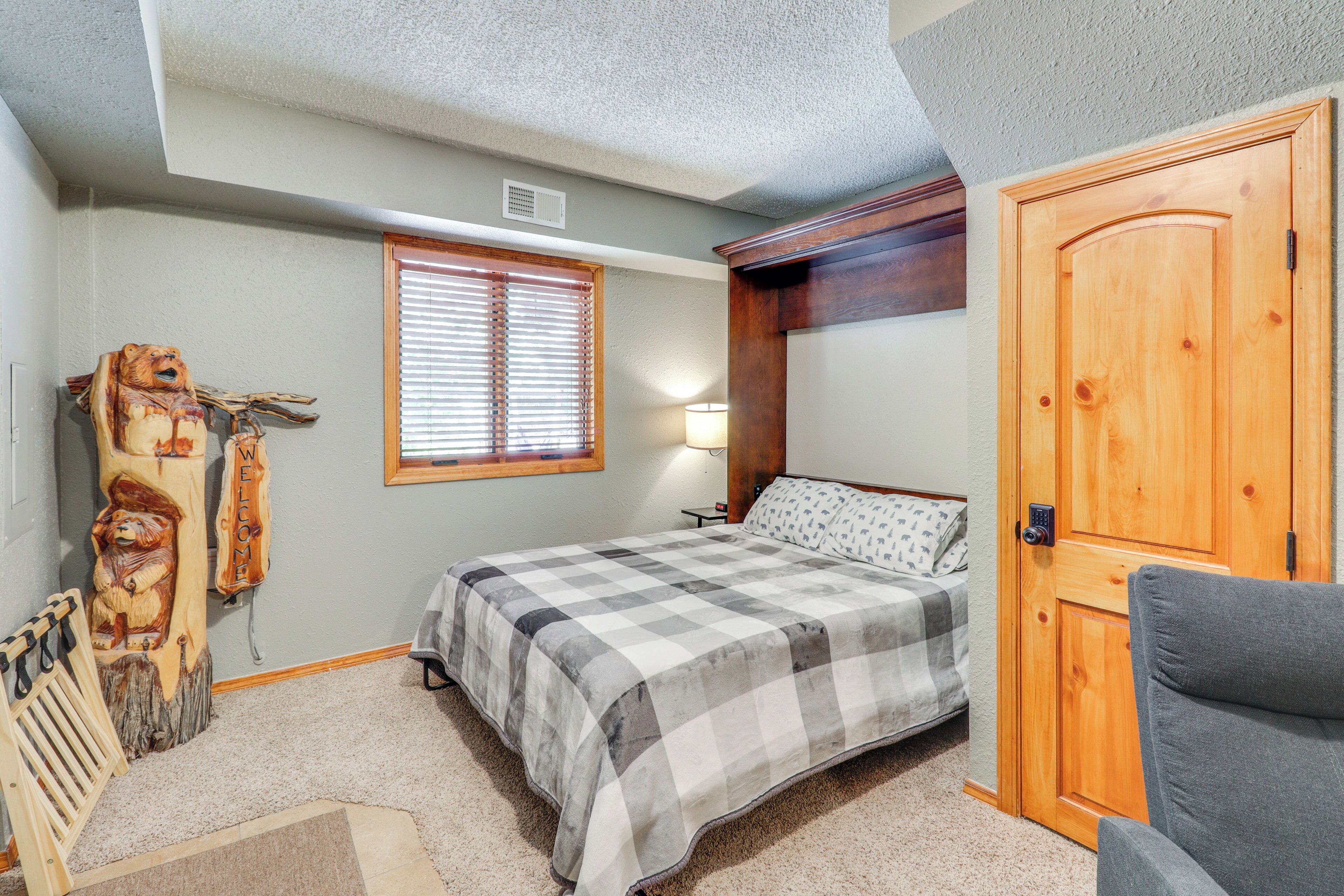 A bedroom with a bed, a wooden door, a window with blinds, a lamp, and a welcome sign.