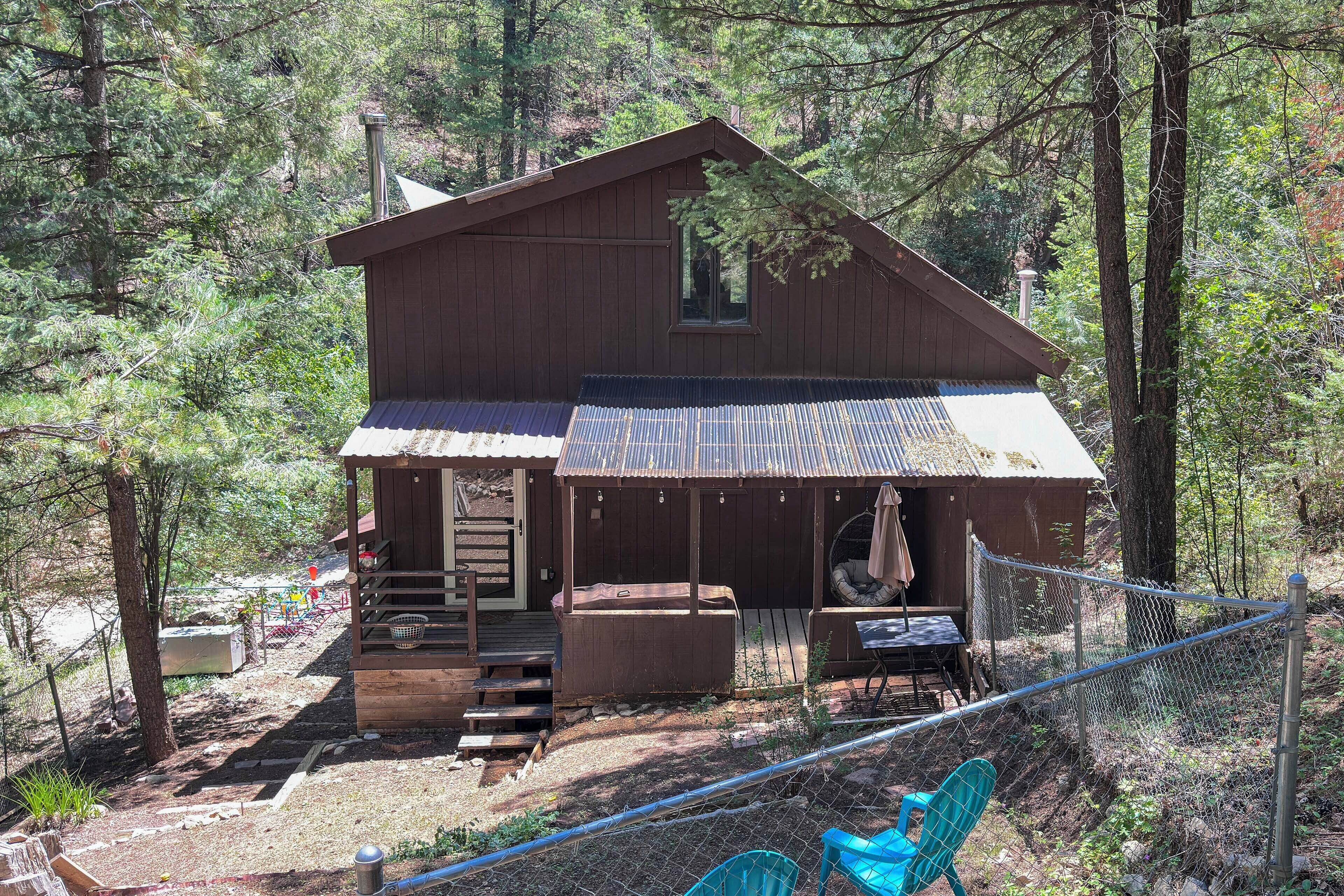A cabin with a porch, a hot tub, and a fenced outdoor area with chairs.