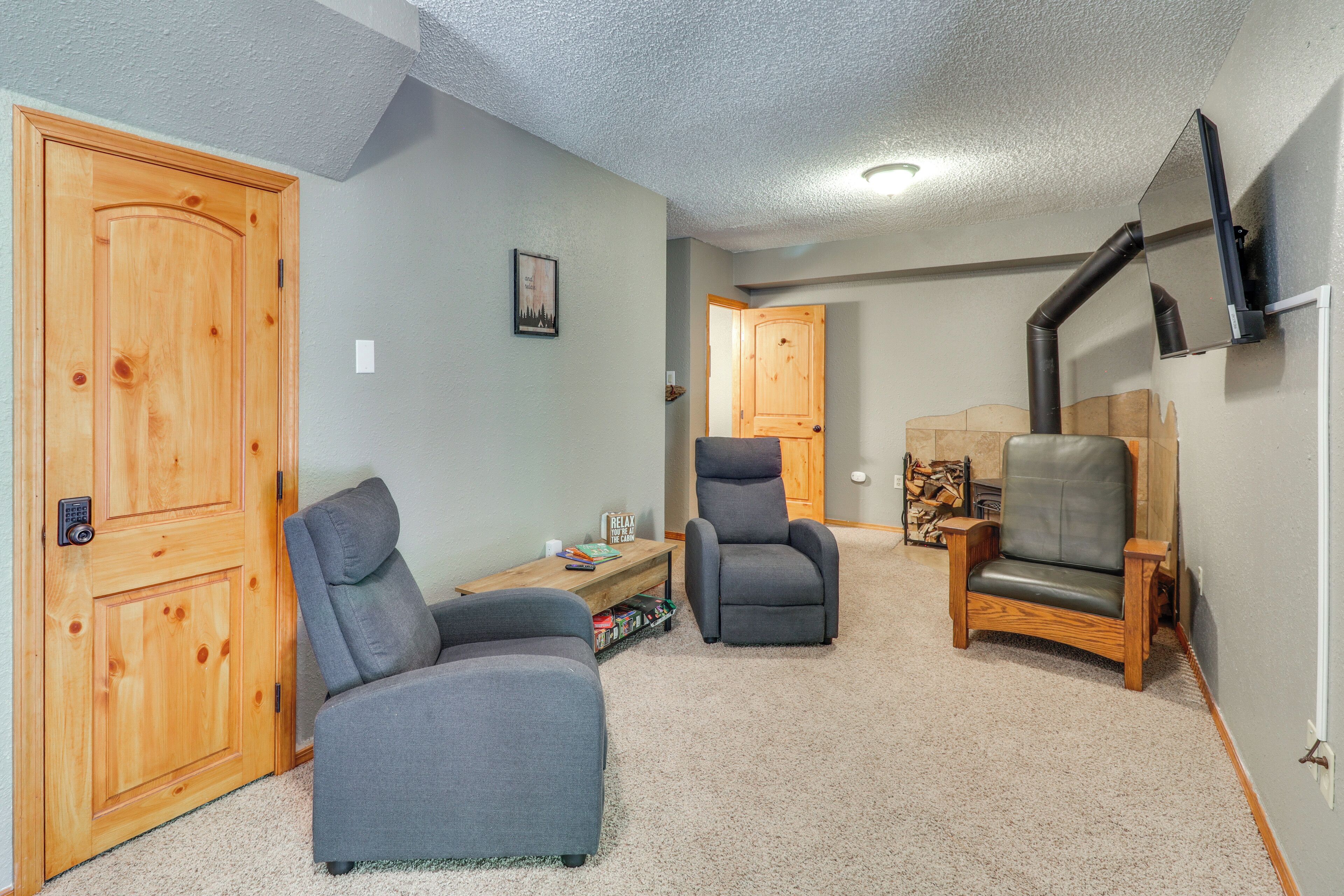 A room with two grey armchairs, a wooden door, a small table with a book, and a mounted TV.