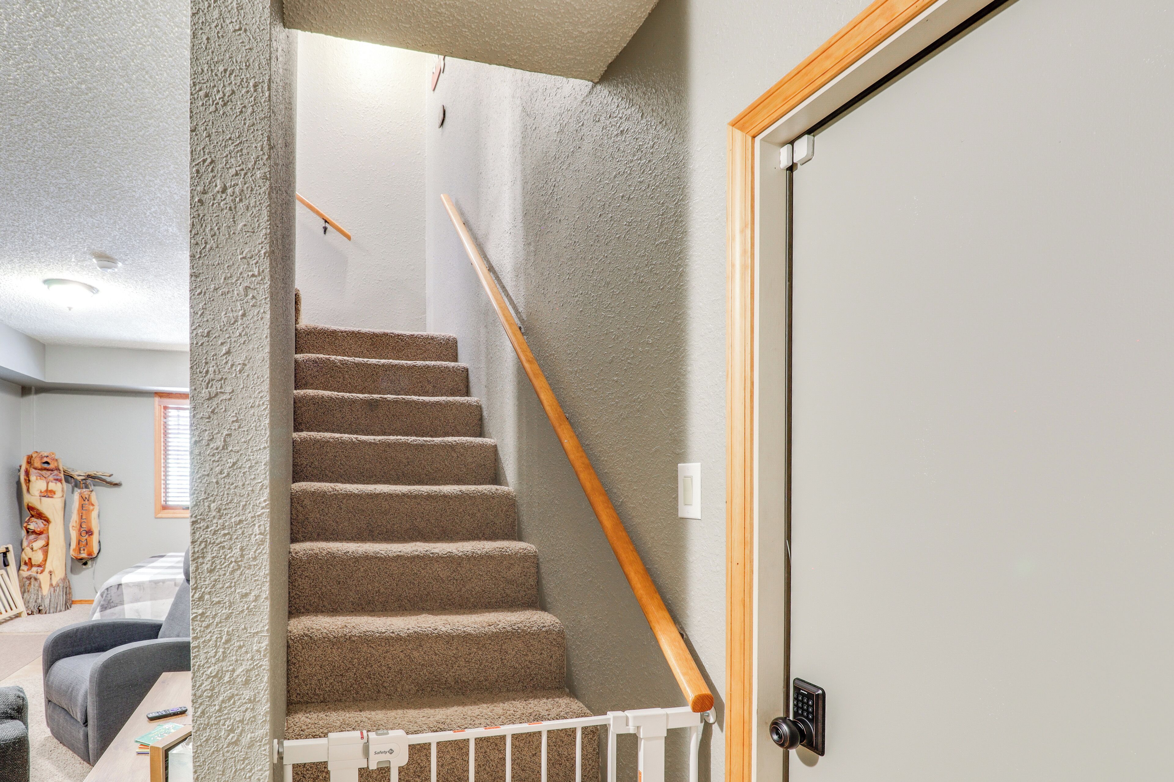 A carpeted staircase with a wooden handrail, a white door with a keyhole, and a safety gate at the bottom.