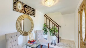 A hallway with a grand staircase, a large ornate mirror, and two upholstered chairs. - Bay & Hill Views: Modern Hercules Home (Hercules)