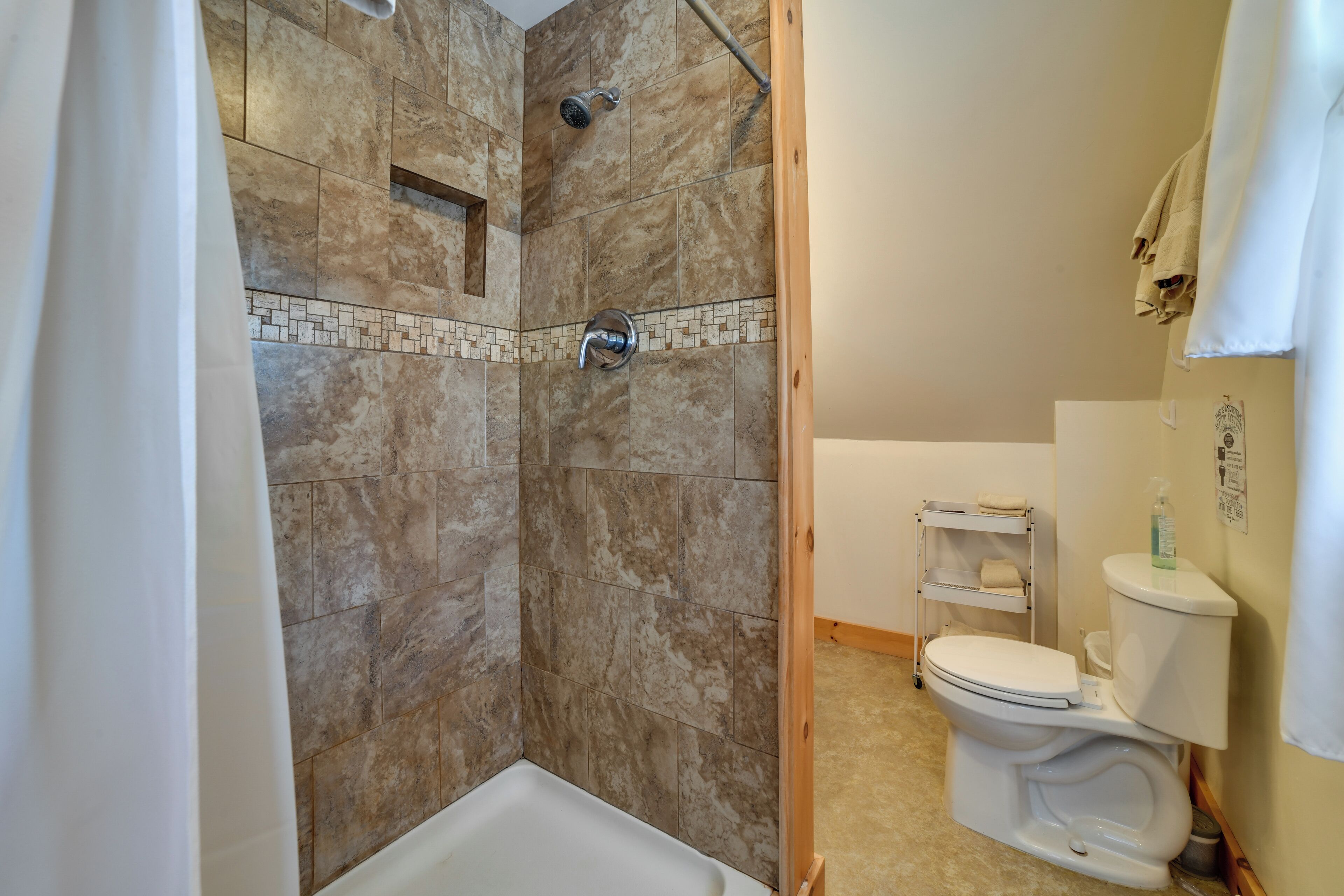Une salle de bain équipée d’une douche, de toilettes et d’une petite étagère où sont rangés les articles de toilette.