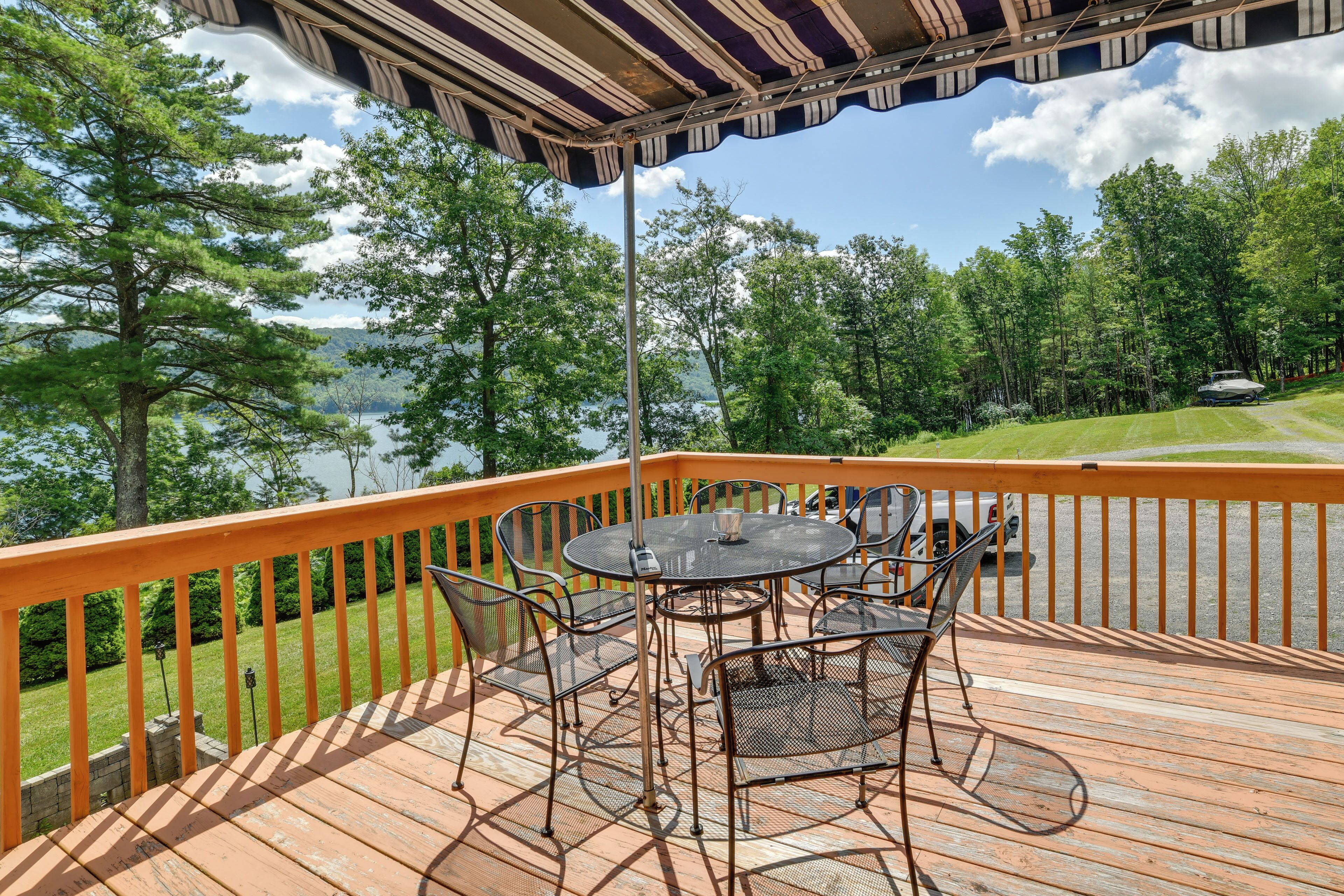 A wooden deck with a metal table and chairs, overlooking a lake and forest.