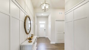 A hallway with white walls, a wooden floor, a white console table with a mirror, and a chandelier. - Recently Built Home w/ View, 3 Mi to Bethany Beach (Ocean View)