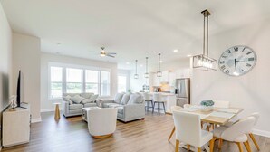 A spacious living room with a sofa, a dining table with chairs, and a kitchen area in the background. - Recently Built Home w/ View, 3 Mi to Bethany Beach (Ocean View)