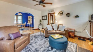 A living room with a brown leather sofa, a blue ottoman, and a ceiling fan. There is a dining area with a wooden table and chairs in the background. - 1 Mi to Riverwalk: Home w/ Fenced Yard in Pueblo (Pueblo)