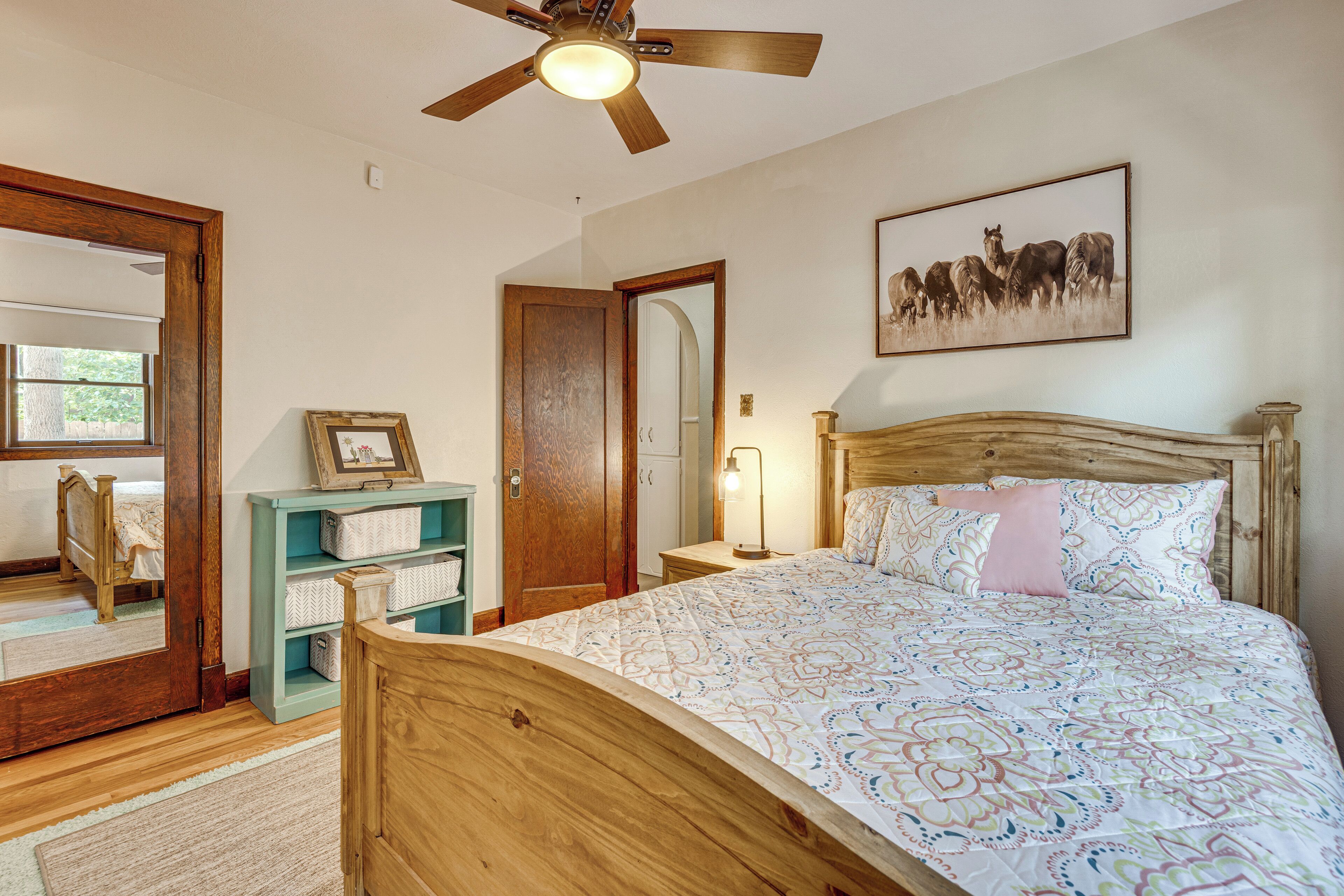 A bedroom with a wooden bed, a ceiling fan, a bedside table with a lamp, a framed picture on the wall, and a window with blinds.