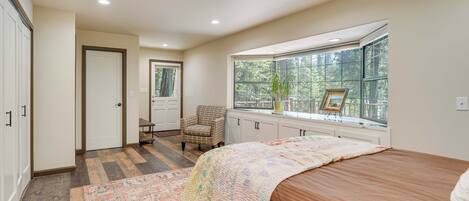 A bedroom with a large window, a bed, a chair, and a rug.