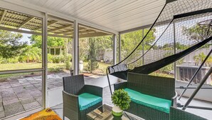 A modern outdoor seating area with wicker furniture and a green cushion, overlooking a garden and a street. - Pet-friendly Home w/ Lanais, Near Dtwn Tampa! (Seffner)