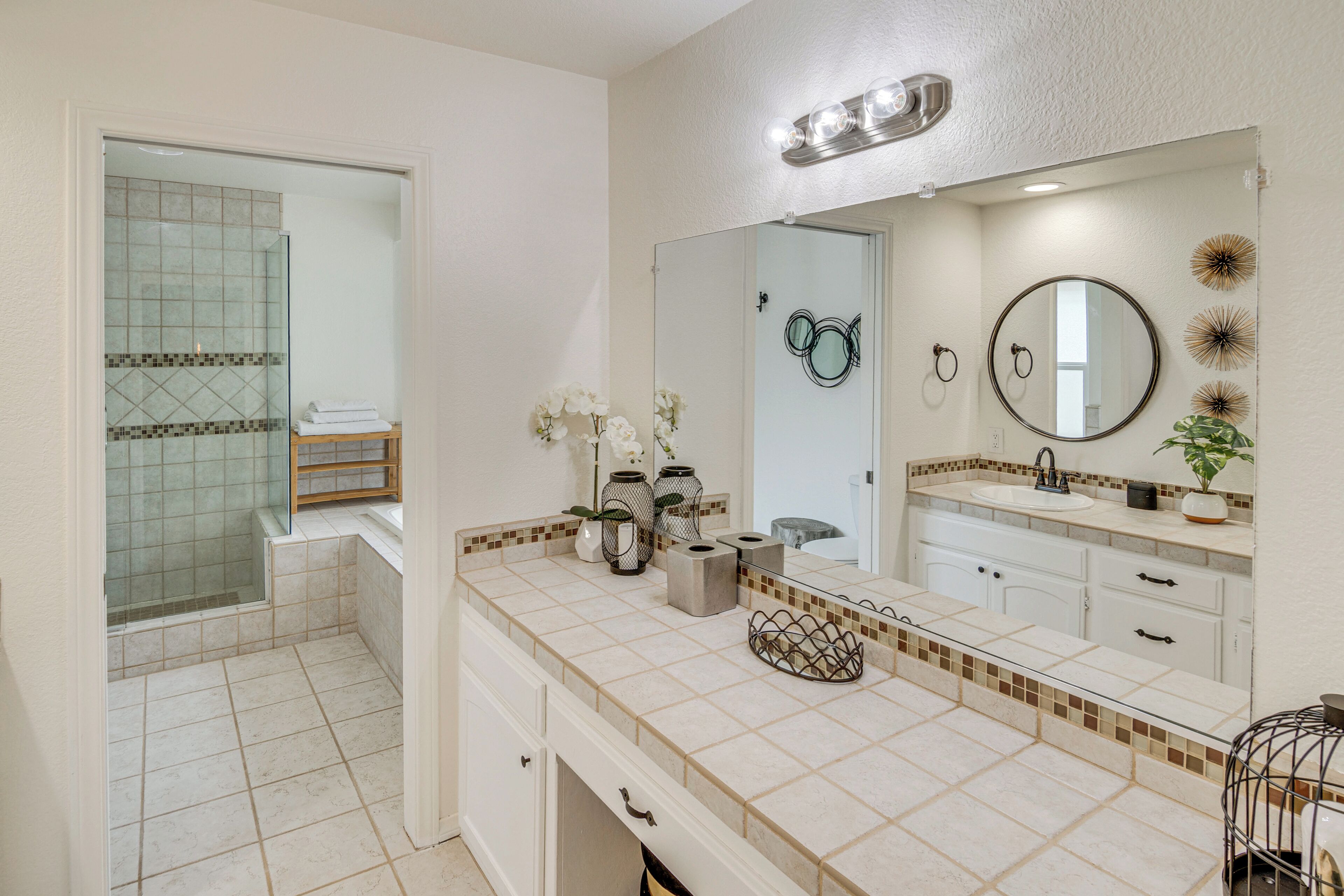 A bathroom with a shower, a sink with a mirror, and a vanity with drawers.