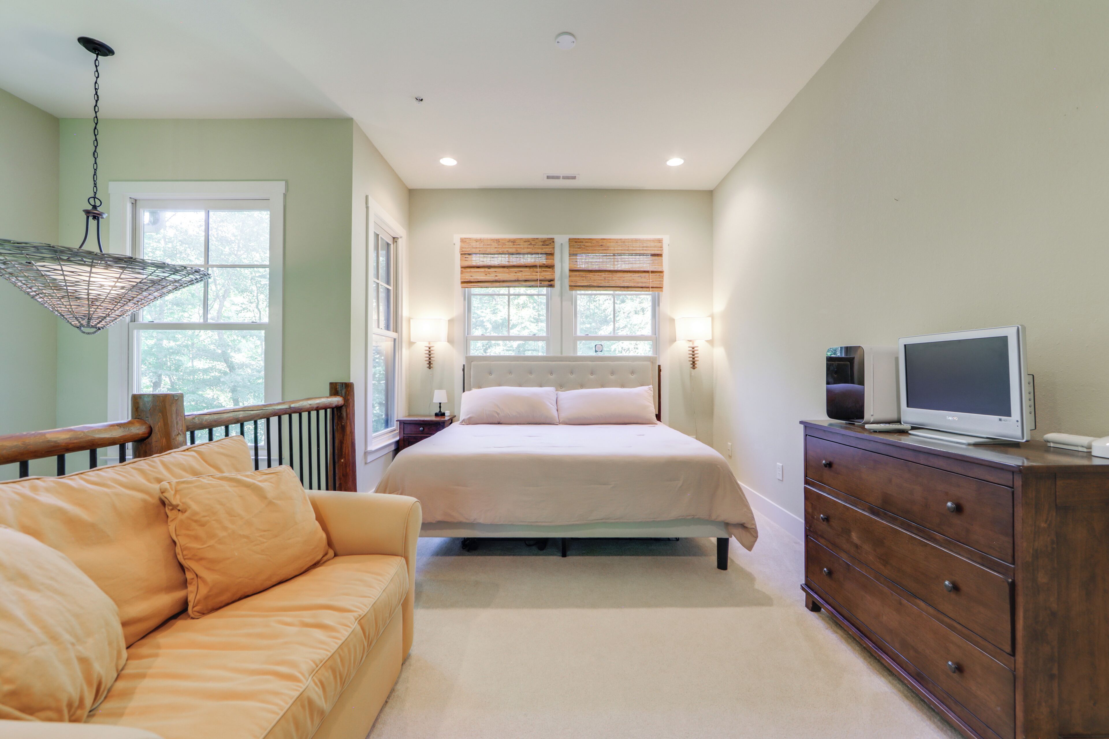 A bedroom with a bed, a wooden dresser, a television, and a hanging light fixture.