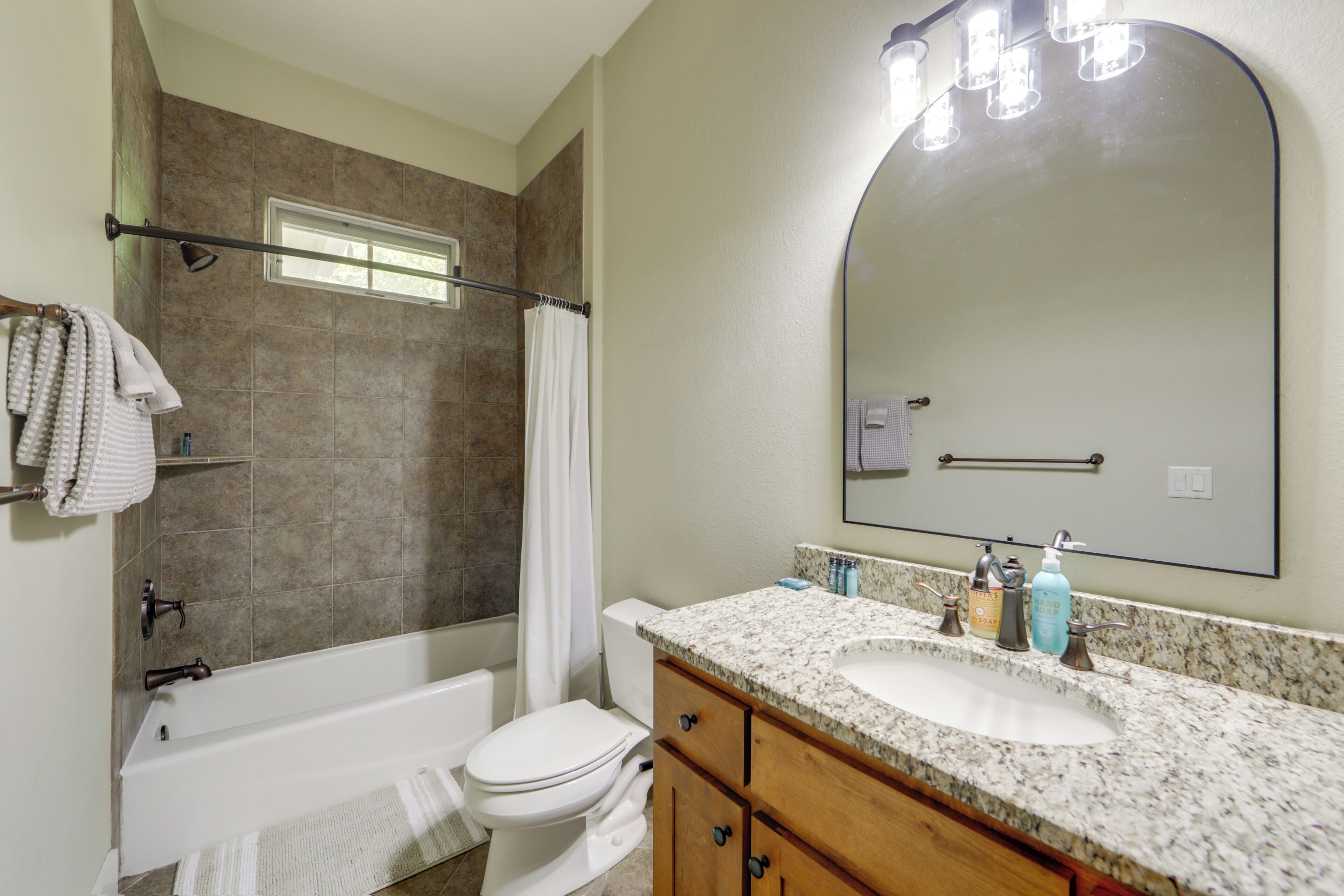 A bathroom with a bathtub, toilet, vanity with a sink, and a large mirror.