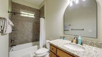 A bathroom with a bathtub, toilet, vanity with a sink, and a large mirror.